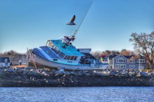 A lobster boat rests on its side up out of the water on a rocky shoreline.