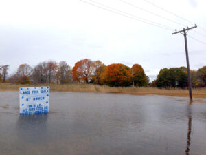 A river over tops its banks and flows by an old mill building.